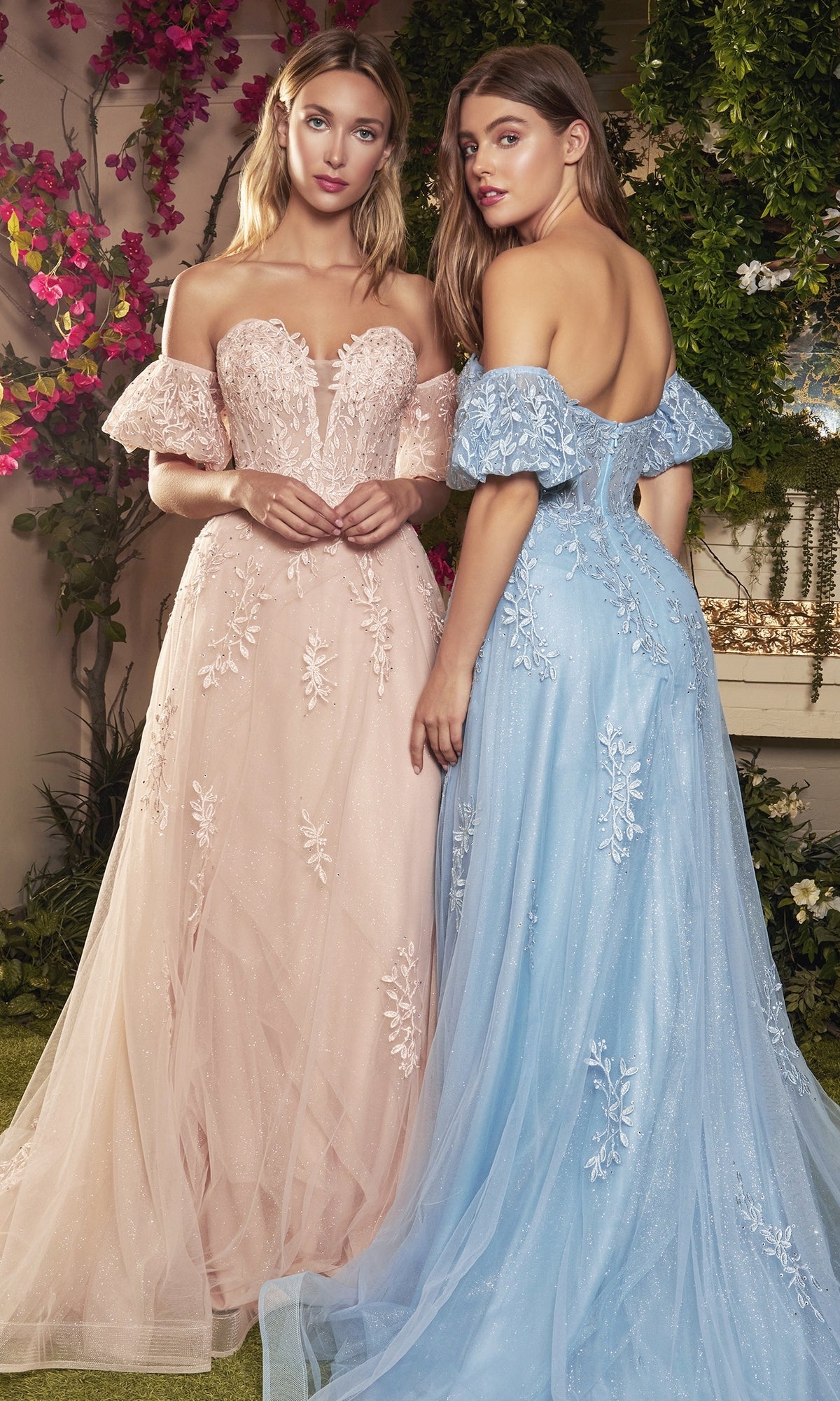 Two women stand side by side in Strapless Puff-Sleeve Long Prom Ball Gown A1046, one in light pink and the other in light blue, both featuring sparkly embroidered floral designs, with flowers and greenery behind them.